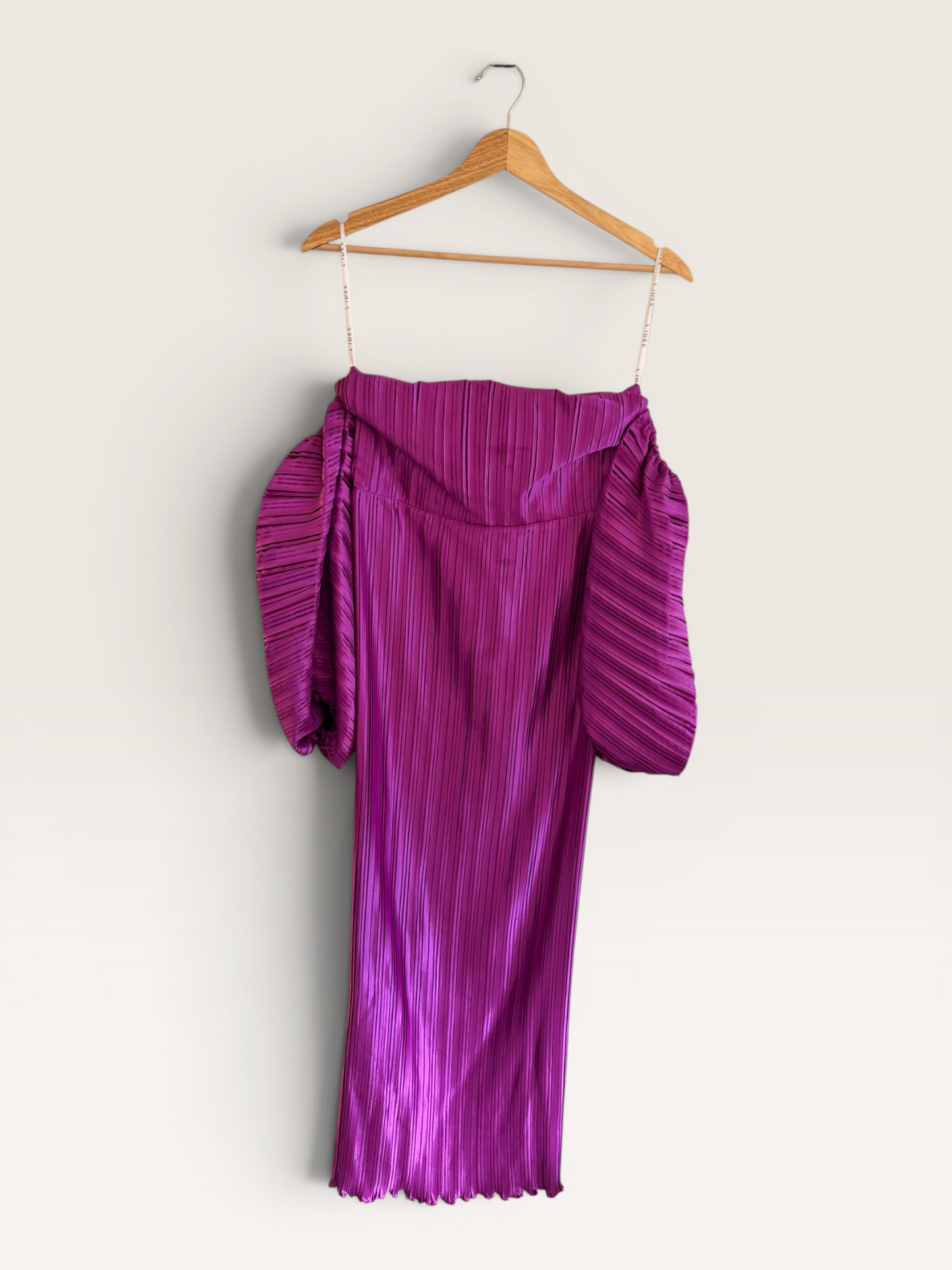 The Runway Reserve magenta pleated off-the-shoulder midi dress with voluminous puff sleeves hanging on a wooden hanger.